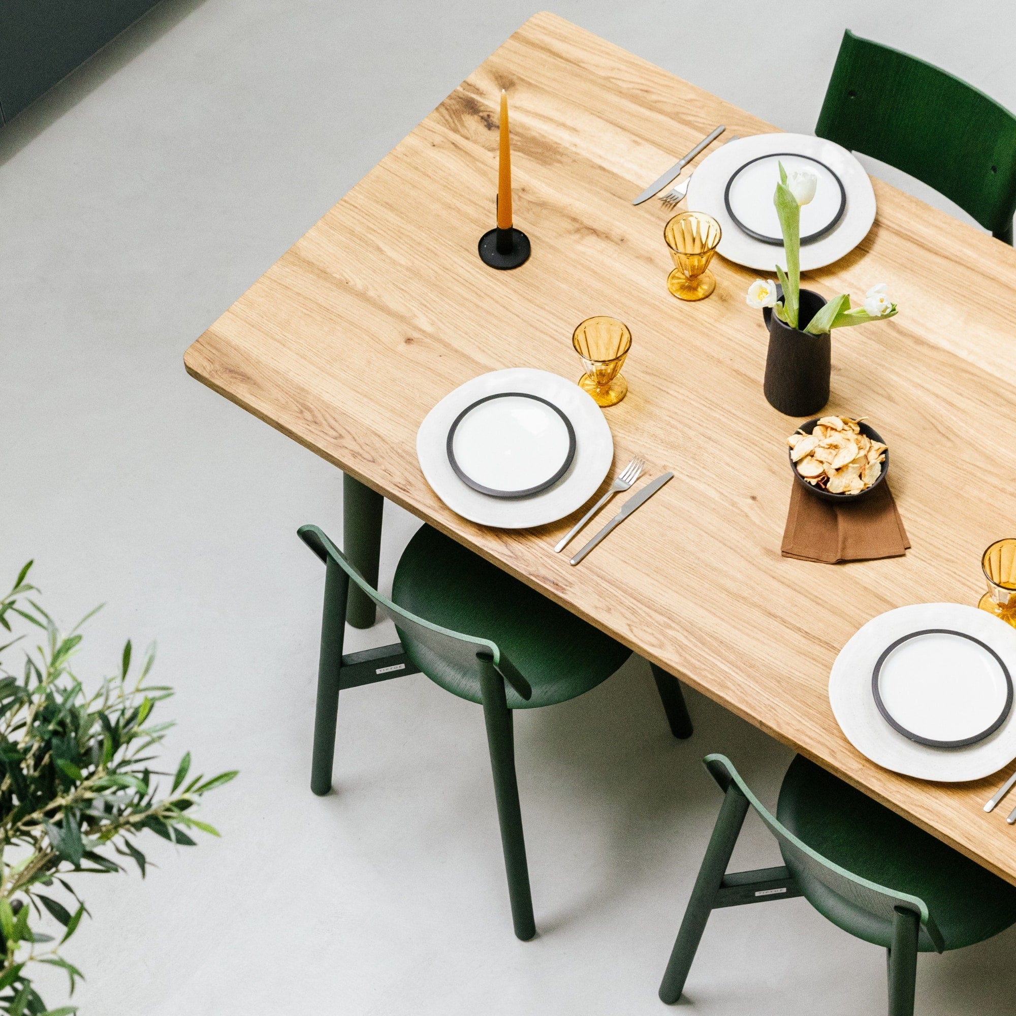 Table en bois recyclé dressée pour quatre personnes, avec vaisselle blanche, verres ambrés et chaises vertes.