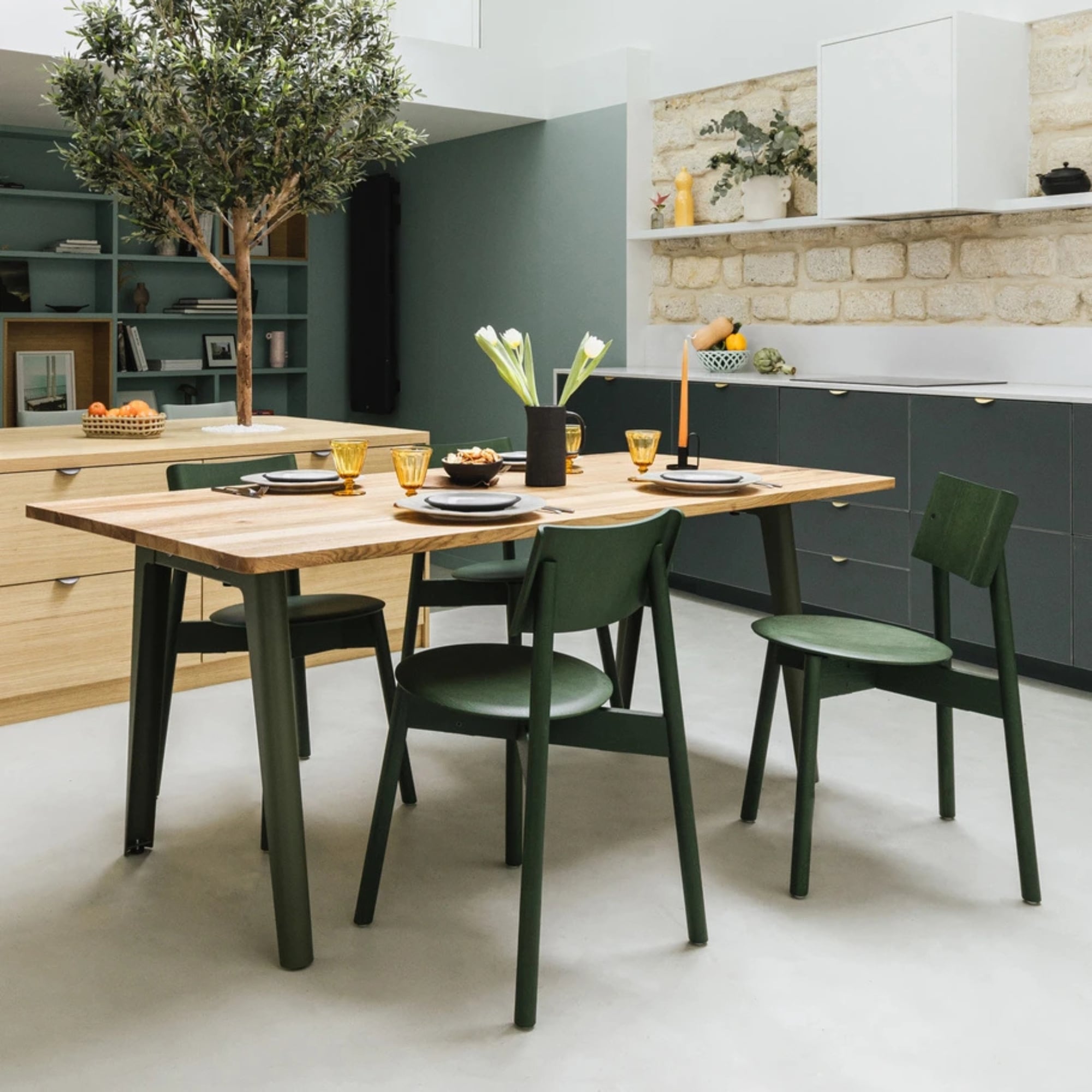 Table en bois recyclé avec pieds gris, assortie de chaises vertes, dressée dans une cuisine moderne lumineuse.