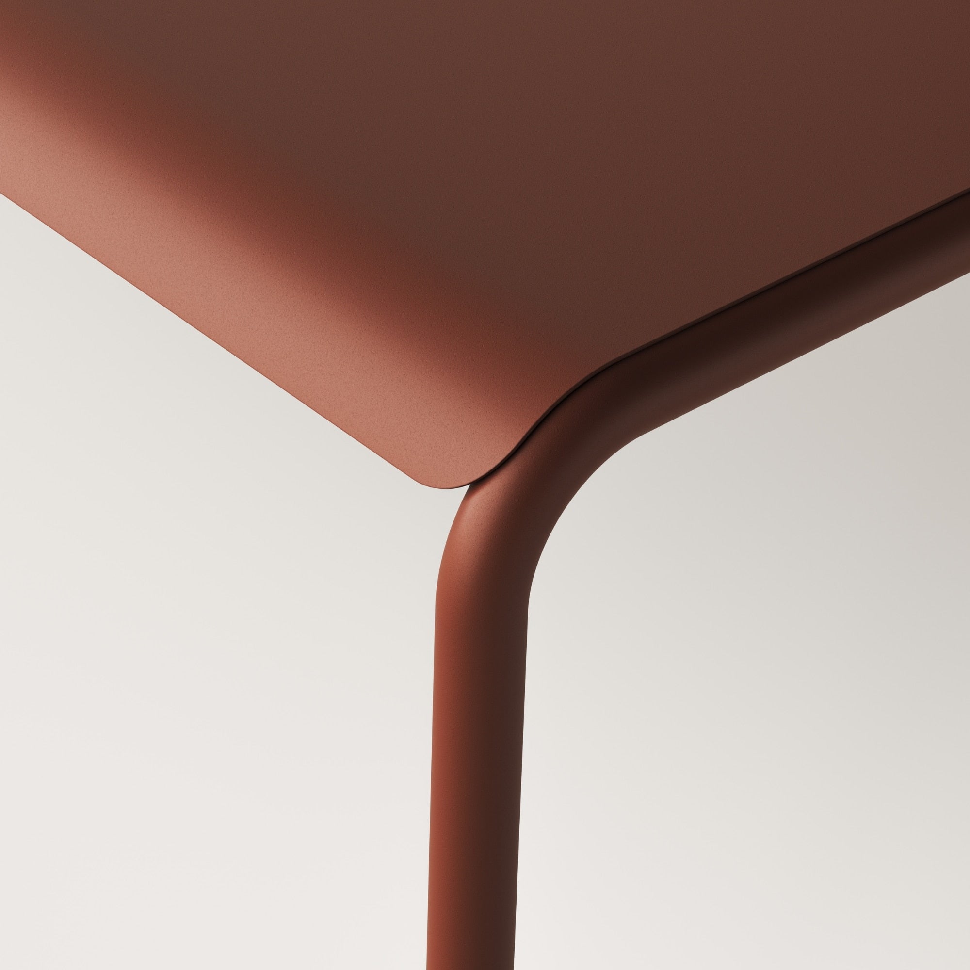 Gros plan sur le coin de la table de jardin, avec des bords arrondis en métal rouge brique, mettant en avant le design moderne et épuré du mobilier extérieur Tiptoe.