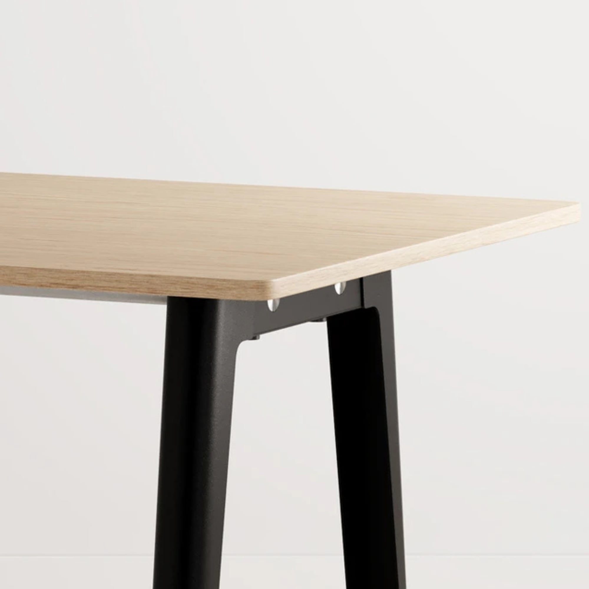 Détail d’un plateau rectangulaire en bois clair avec piètement en métal noir, sur fond blanc uni