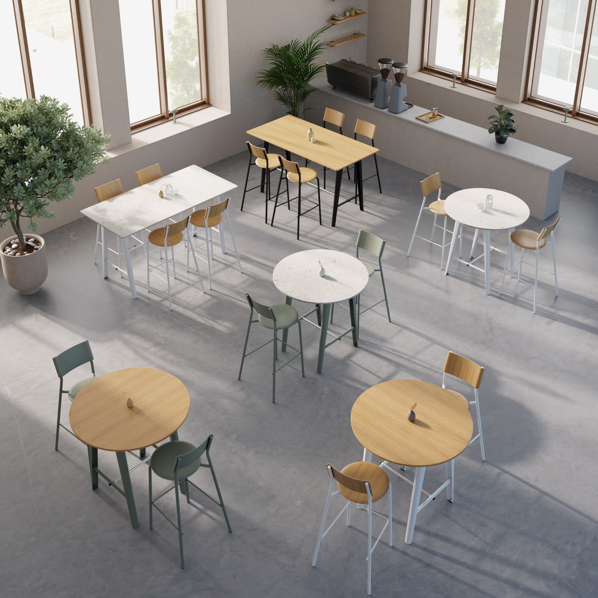 Tables hautes rondes et rectangulaires disposées dans un café lumineux, sur fond de sol en béton et grandes fenêtres.