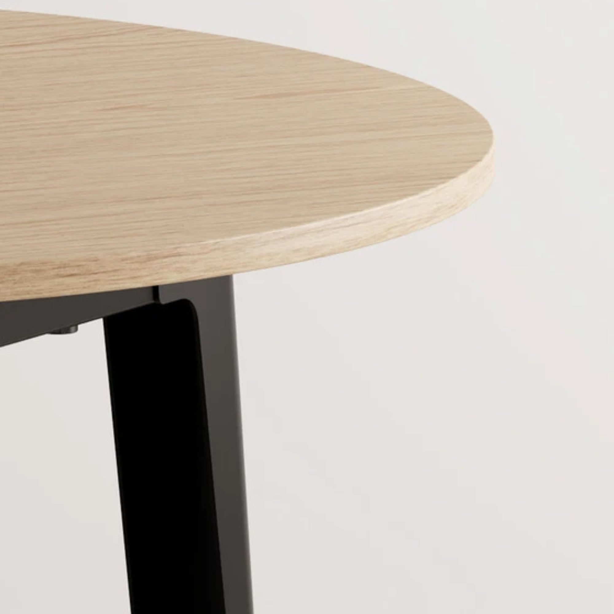 Zoom sur le plateau arrondi en chêne clair d’une table haute avec pied en métal noir, sur fond blanc
