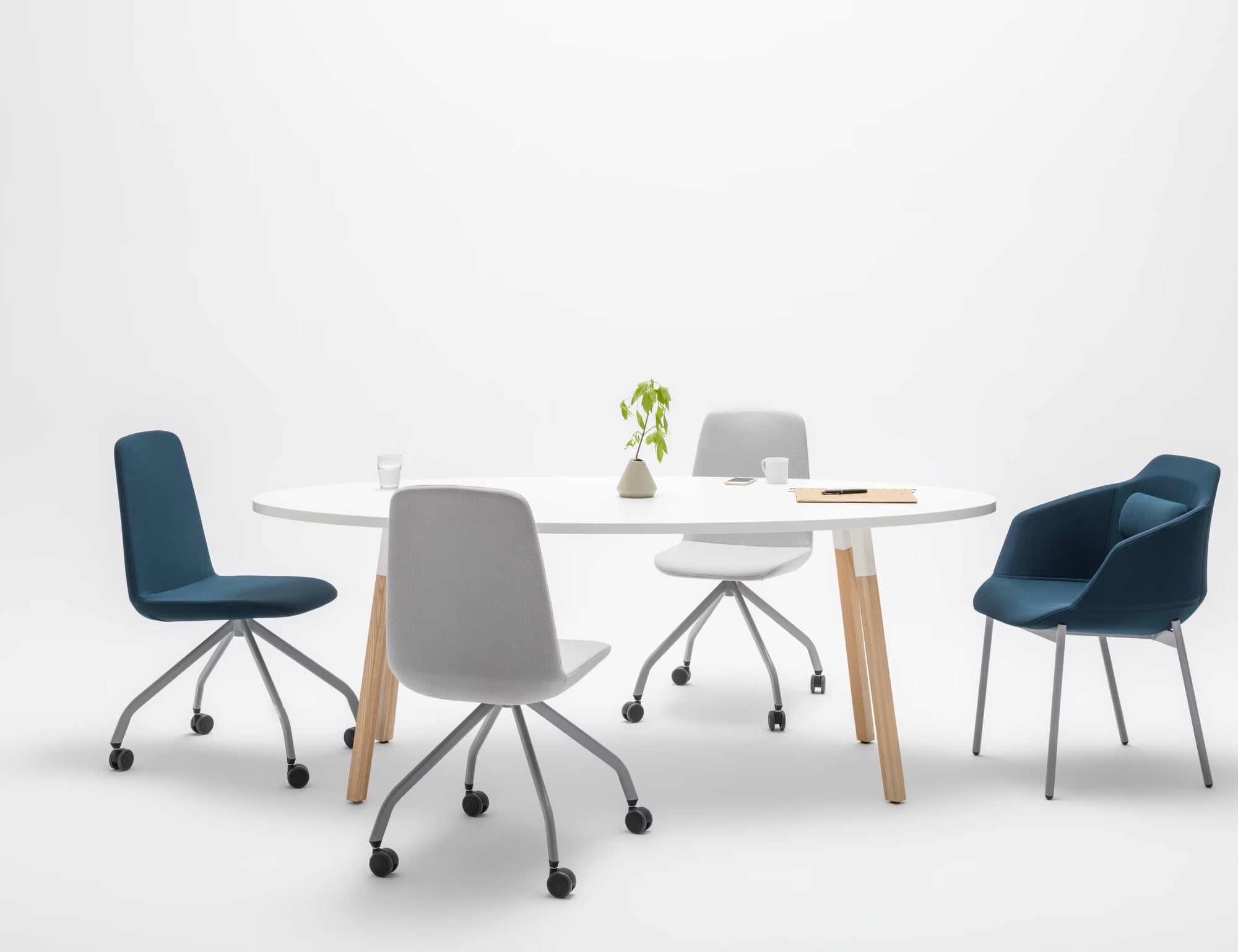 Table ovale blanche entourée de chaises grises et bleues, ambiance moderne et épurée sur fond blanc.
