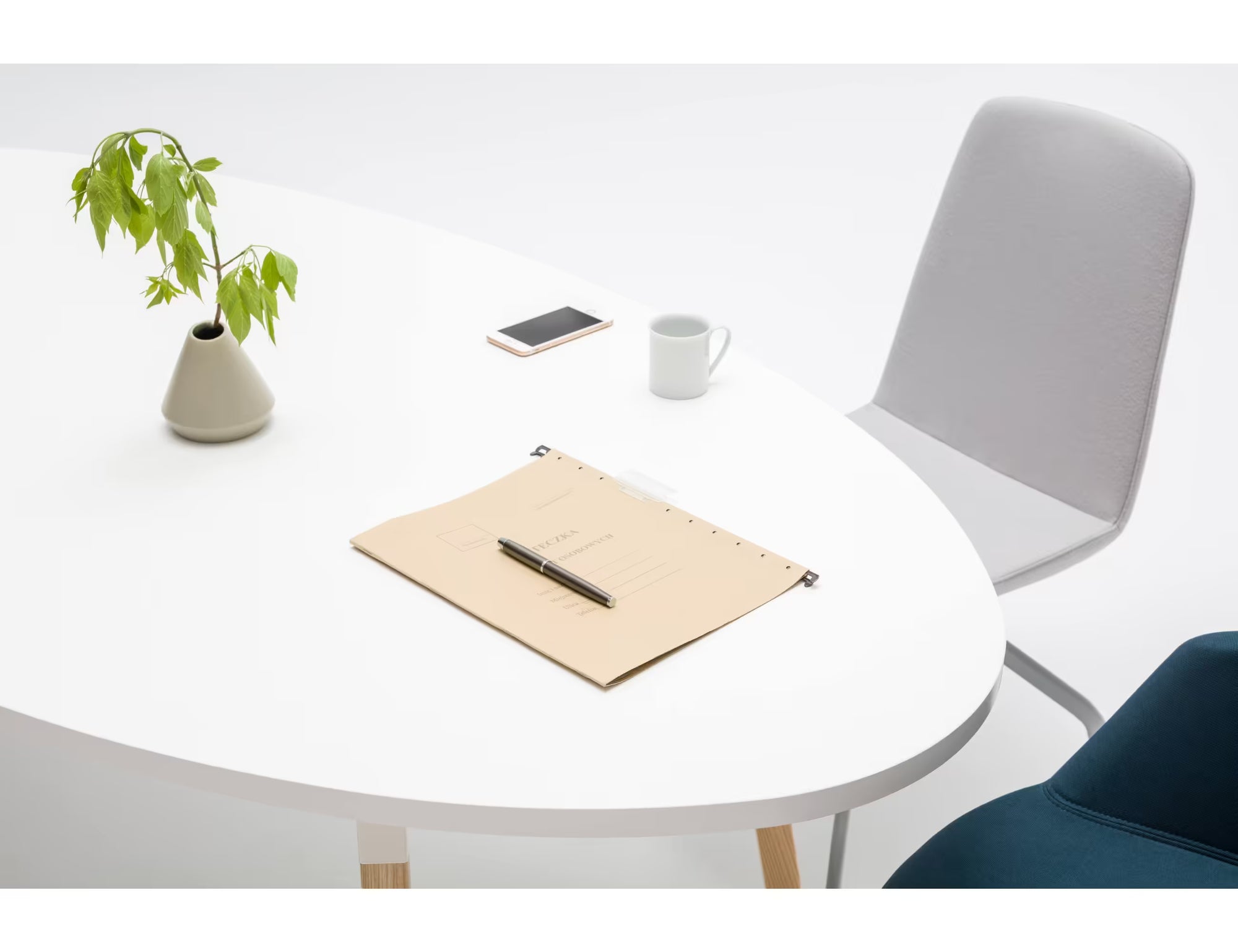 Table blanche ovale avec vase et plante, dossier gris et carnet posé, ambiance minimaliste et lumineuse.