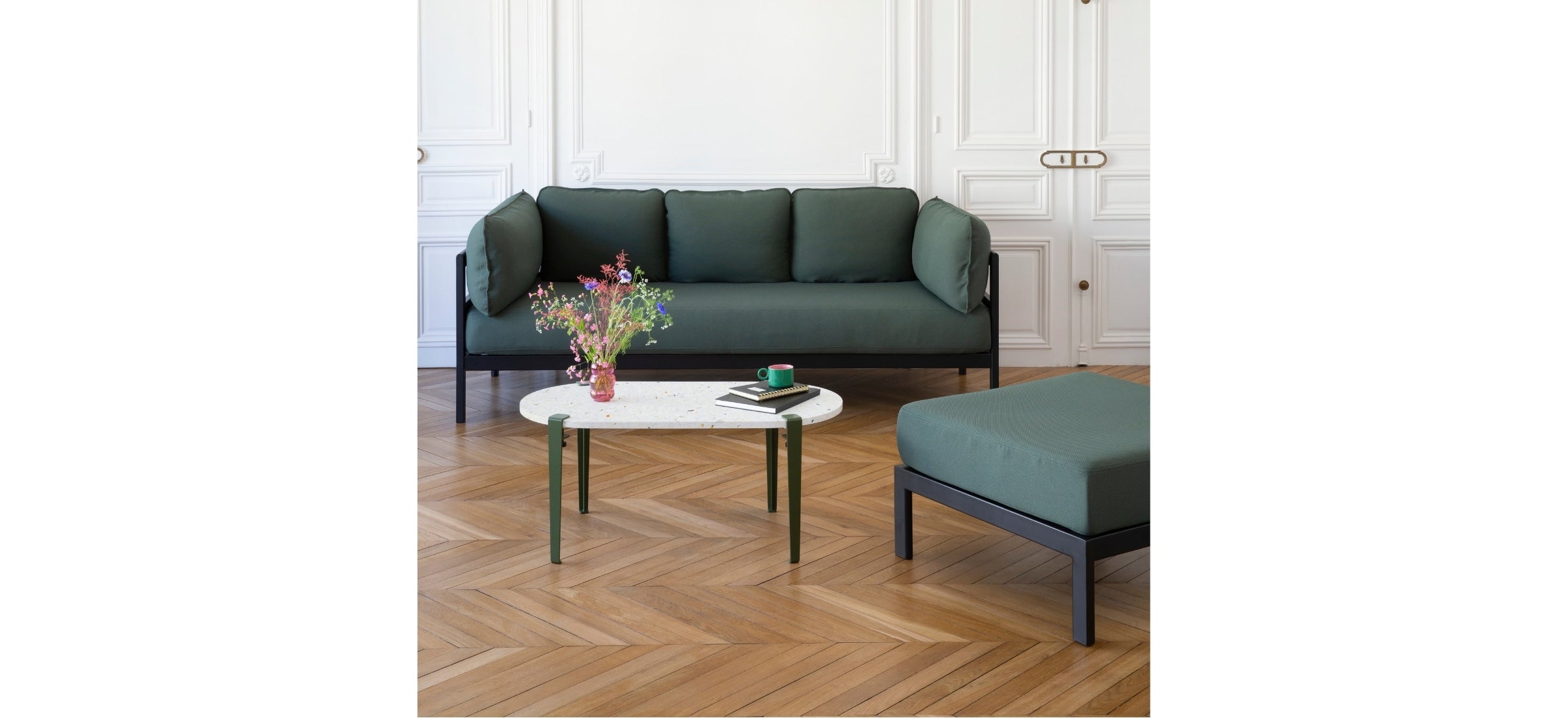 Canapé Easy 3 places vert forêt avec pouf assorti, installé dans un salon lumineux à parquet en chevrons, accompagné d’une table basse en terrazzo.