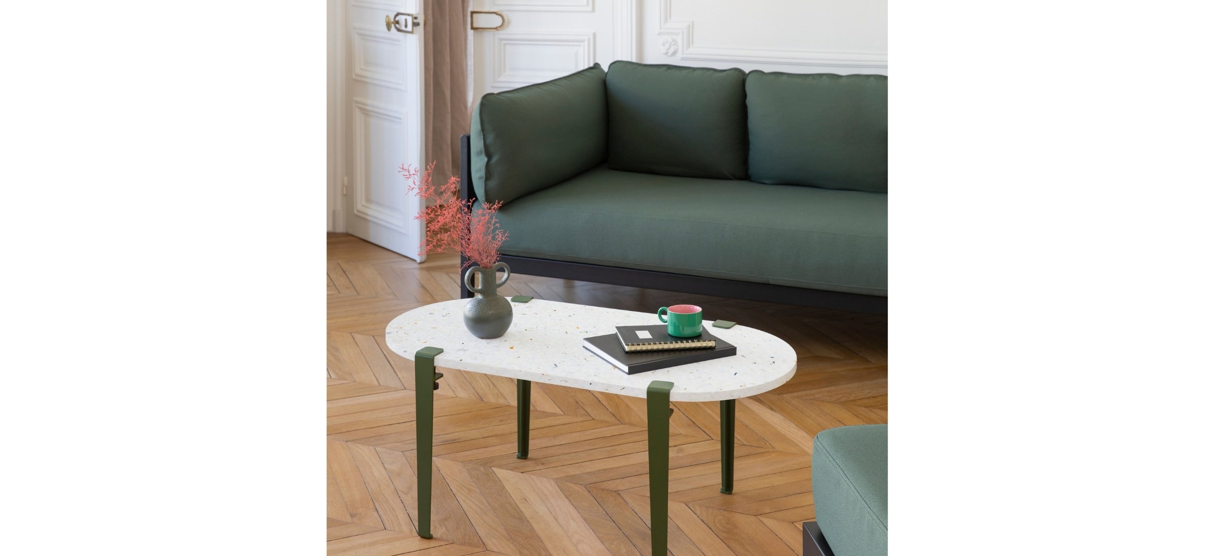 Canapé Easy vert forêt avec table basse en terrazzo et pieds verts, posé sur un parquet en chevrons.