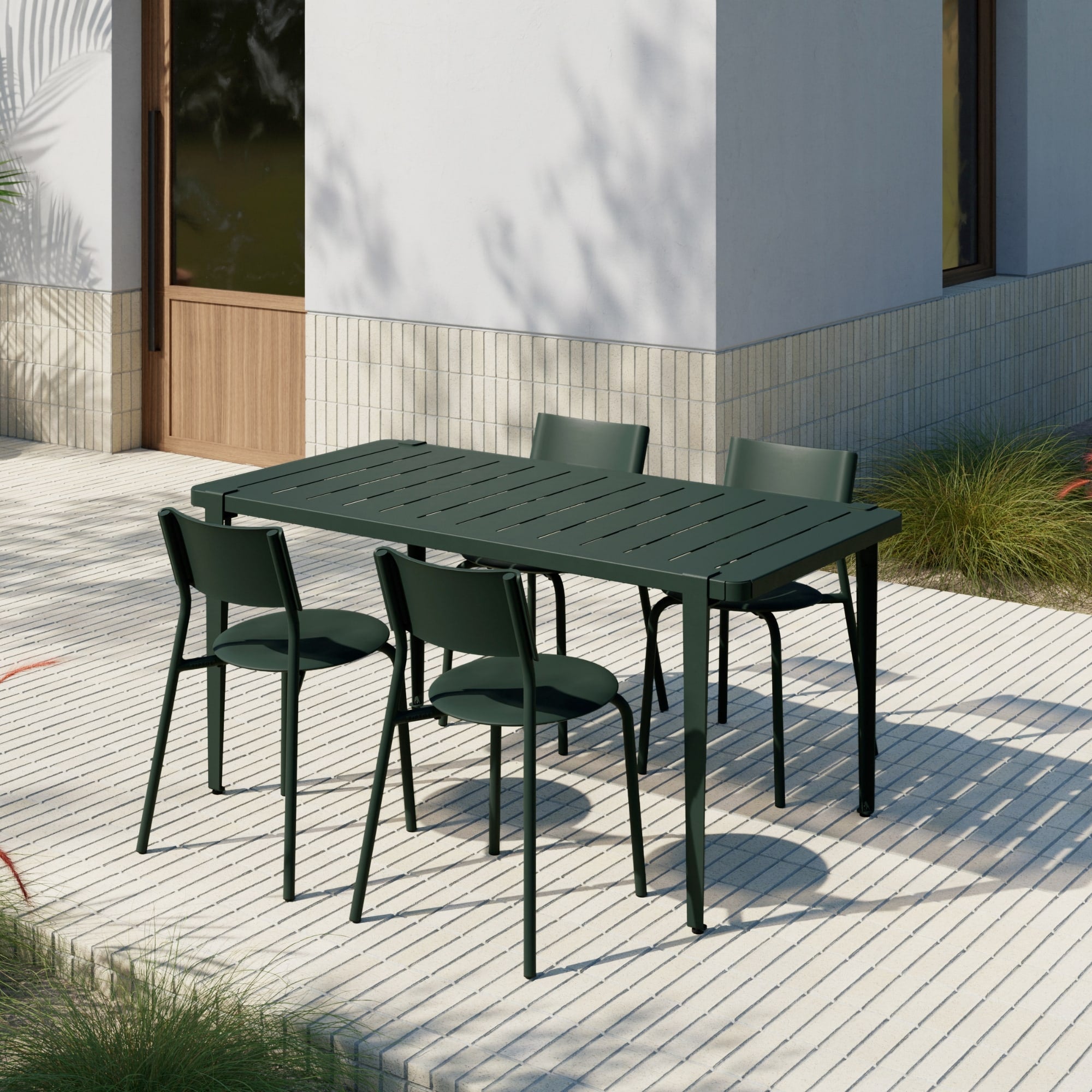 Table de jardin verte Tiptoe avec six chaises assorties, installée sur une terrasse en dalles claires à l’ombre d’une façade moderne.